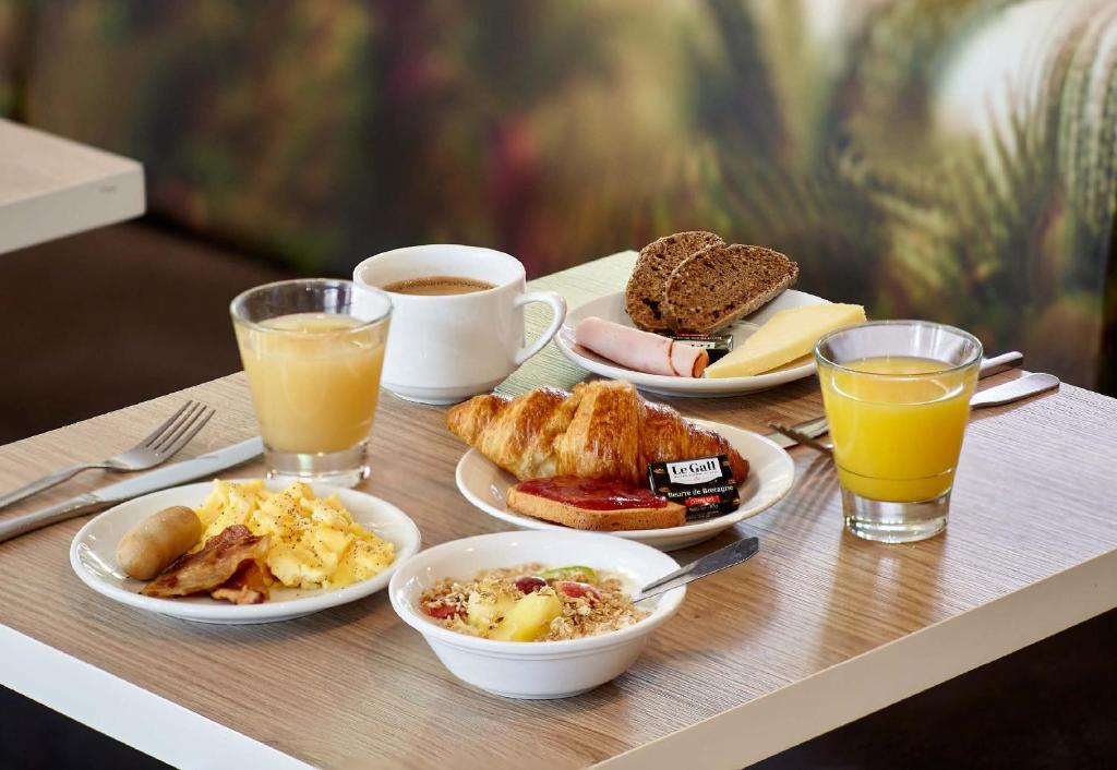 una mesa cubierta con platos de comida y bebida para el desayuno en B&B HOTEL Maubeuge Gare, en Maubeuge