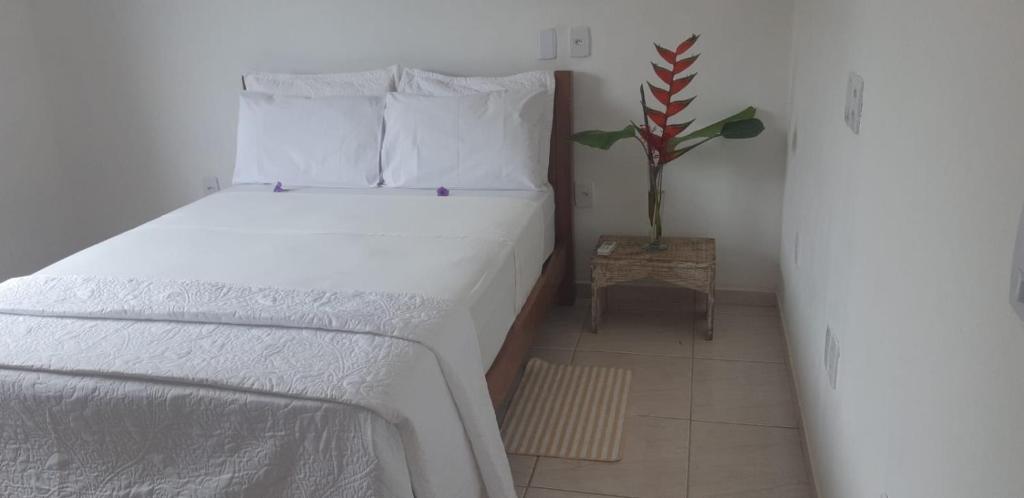 um quarto com uma cama com lençóis brancos e uma planta em Casa Flor em Antônio Cipriano