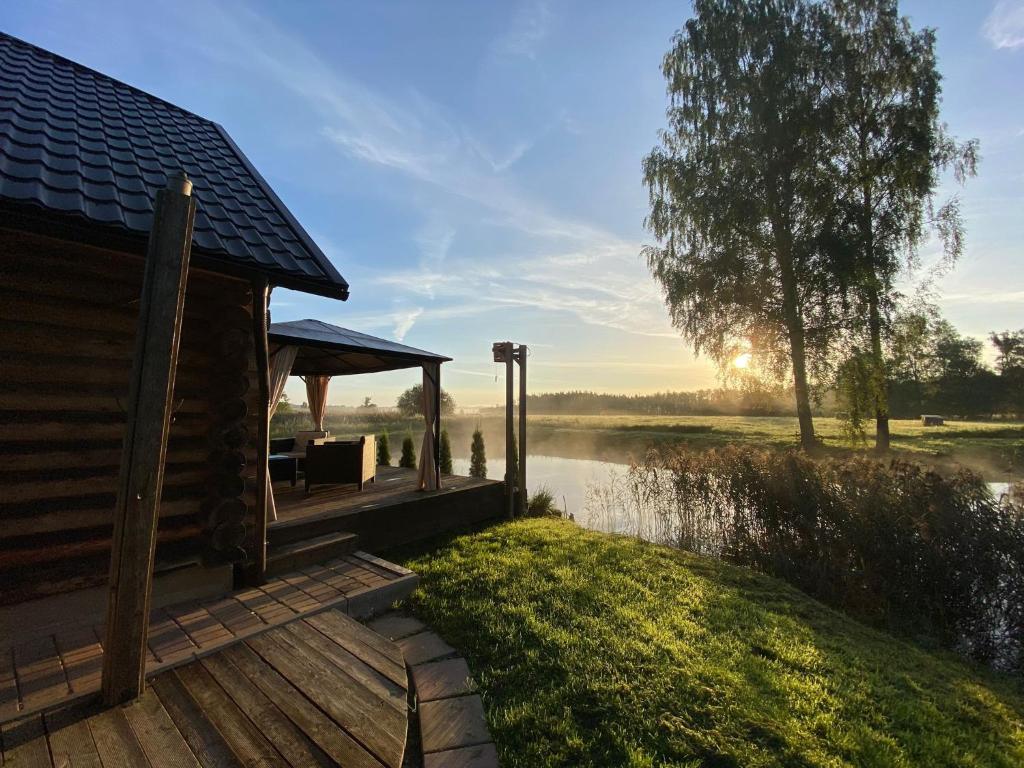 une cabine avec une terrasse à côté d'une masse d'eau dans l'établissement Cabin with a sauna& pond+a hot Tub(additional fee), à Ķeņini