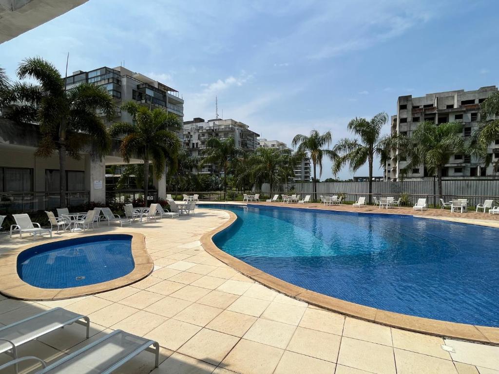 a swimming pool with chairs and palm trees and buildings at Apartamento Rio Marina Resort in Mangaratiba