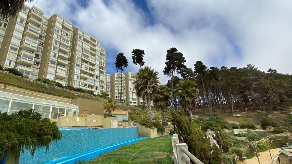 un grand immeuble avec piscine et palmiers dans l'établissement Condominio Pinares del Canelillo, à Algarrobo