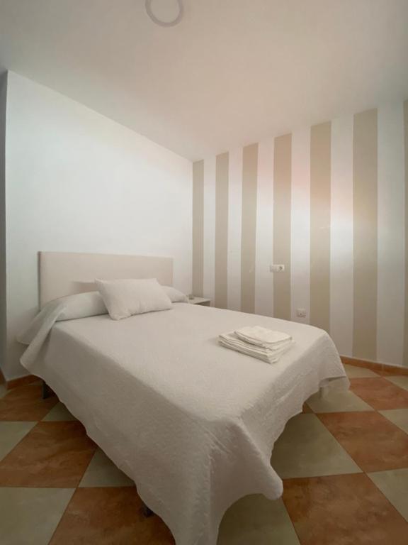 un letto bianco in una stanza con pareti a strisce di Asís 20.2 a Medina Sidonia