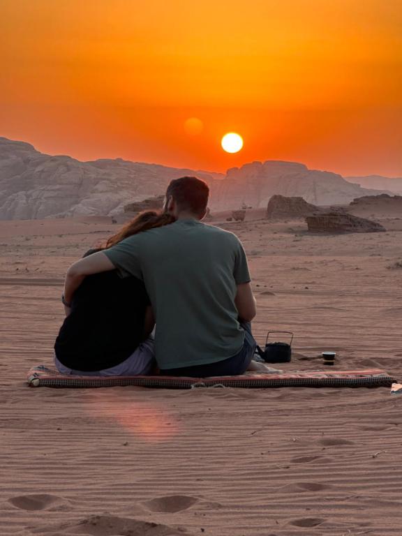 Um homem e uma mulher sentados no deserto a ver o pôr-do-sol. em Sunset Dreams camp em Wadi Rum