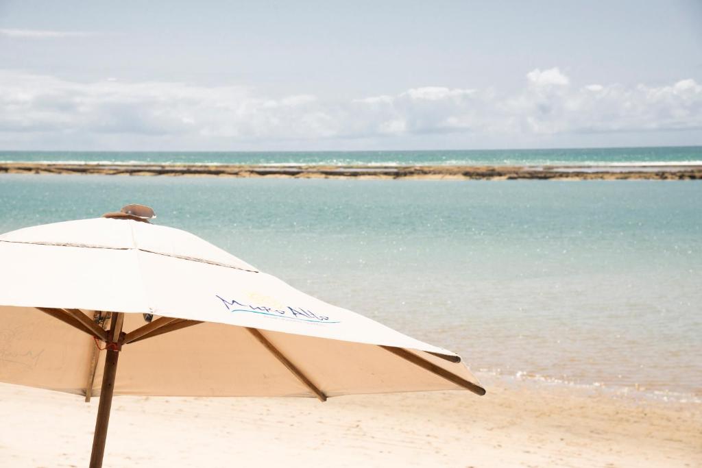 un ombrellone bianco seduto su una spiaggia vicino all'oceano di Flat Marupiara, no melhor trecho da praia de Muro Alto, beira-mar com piscina, equipado, varanda, restaurante, estacionamento e wi-fi, a 10' de carro de Porto de Galinhas a Porto De Galinhas