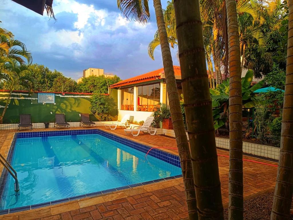a swimming pool with palm trees in front of a house at POUSADA EVELINA in Foz do Iguaçu