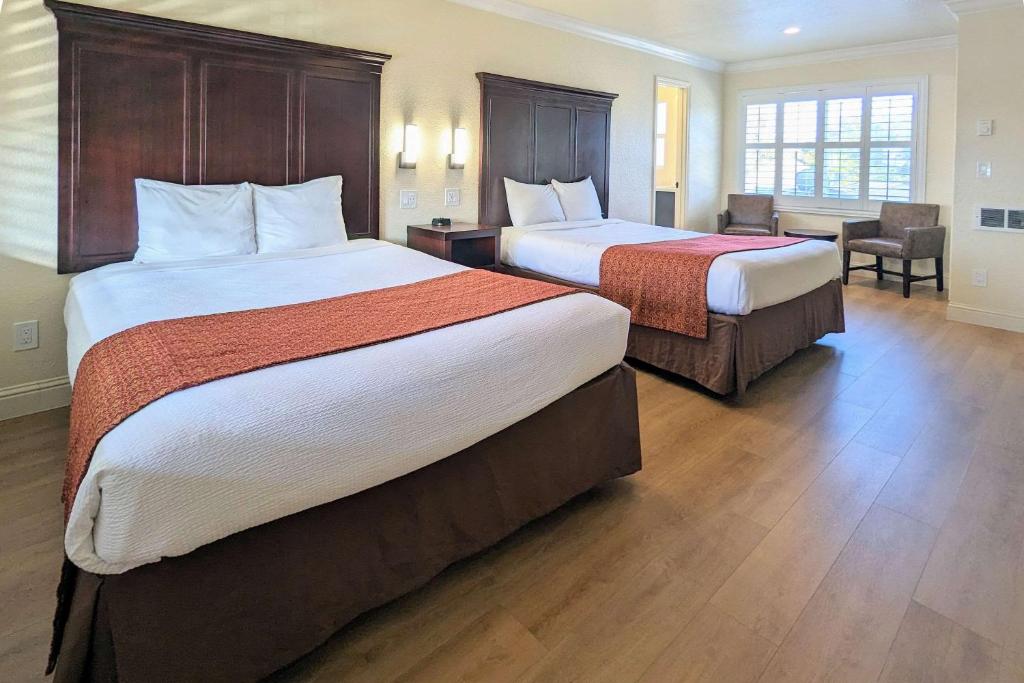 a hotel room with two beds and a desk at Clarion Collection Wilkie's Inn Pacific Grove - Monterey in Pacific Grove