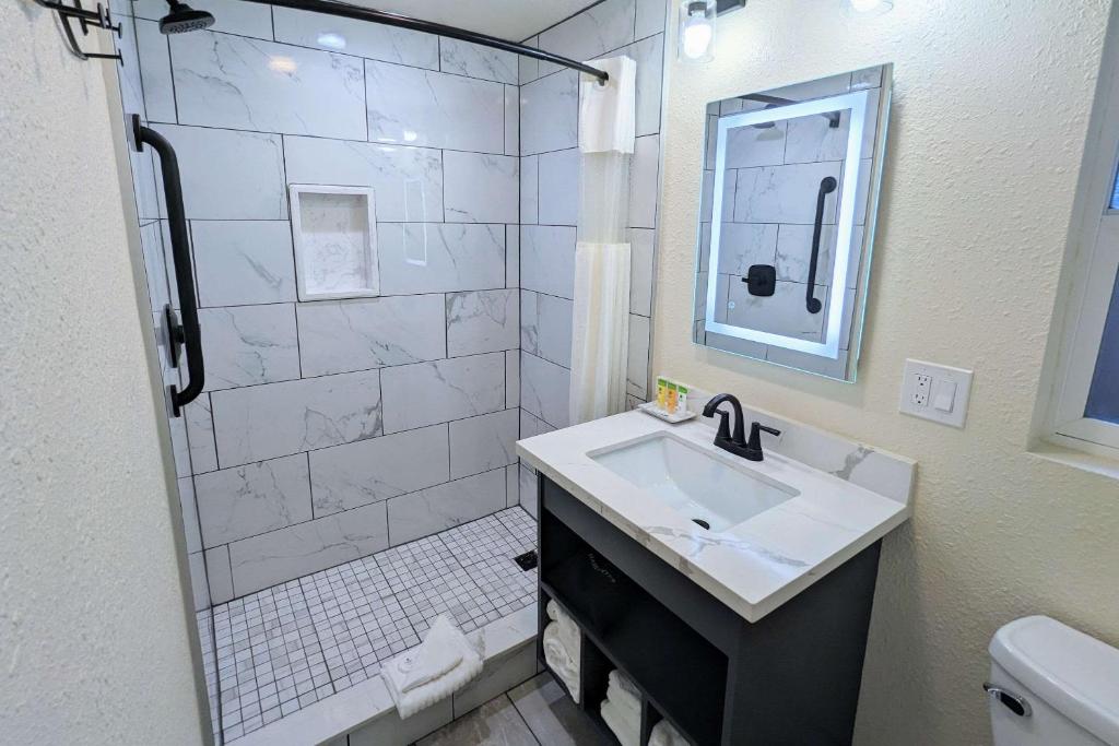 a white bathroom with a sink and a shower at Clarion Collection Wilkie's Inn Pacific Grove - Monterey in Pacific Grove