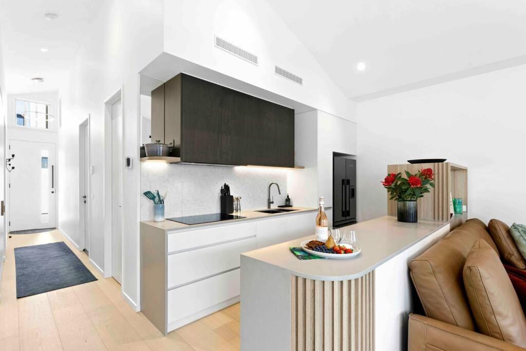 a white kitchen with a counter top and a couch at Mod House Ocean Grove- Walk to the shops, cafes, beach and park! Brand new luxury apartment in gated complex in Ocean Grove