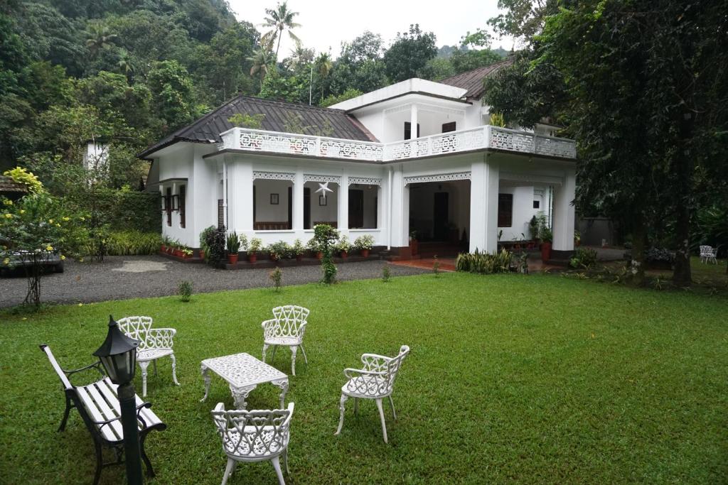 a white house with chairs and a table in the yard at Vanilla County Heritage Plantation Bungalow in Vagamon