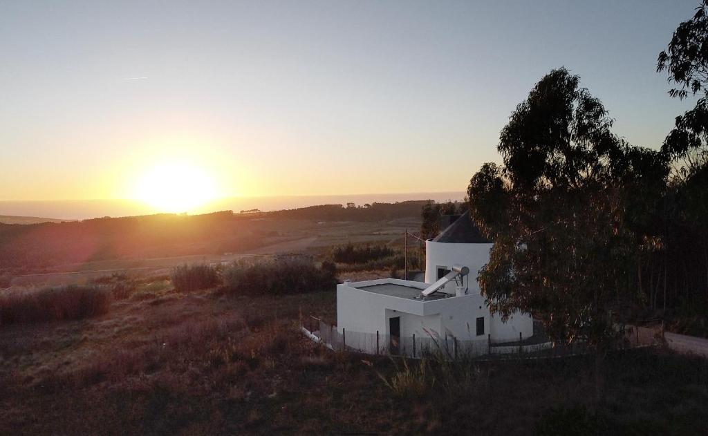a white house in a field with the sunset in the background at O Moinho 98 - A cozy getaway by the coast in Lourinhã