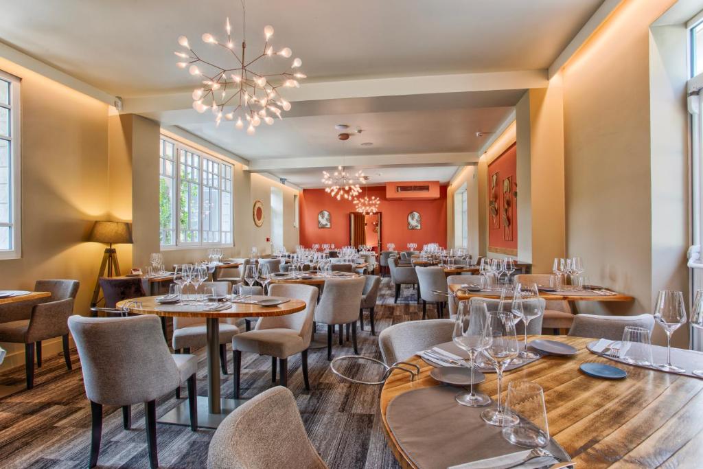 カブールにあるLe Castel Cabourg hôtel & SPA- Restaurant La Calypsoのテーブルと椅子、シャンデリアのあるレストラン
