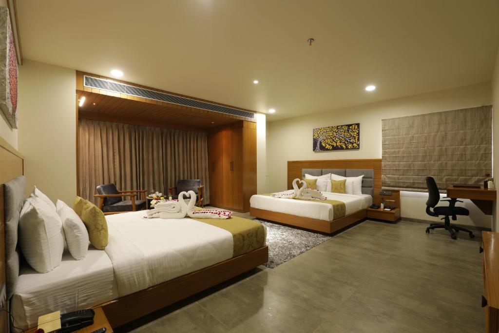 a hotel room with two beds and a desk at Tara Suns in Vadodara