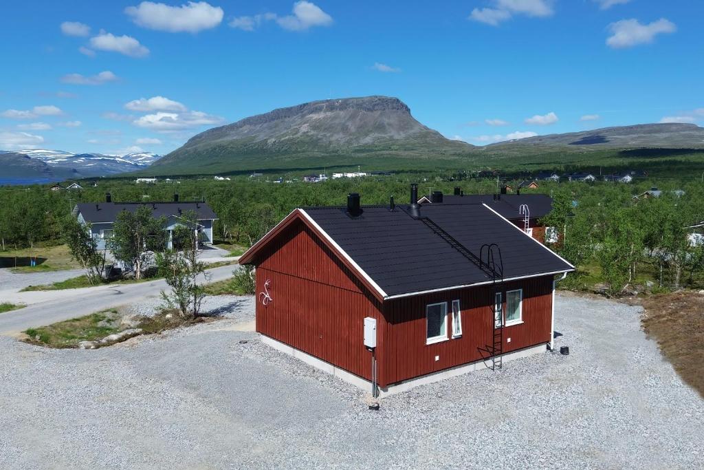 a red house with a black roof in a parking lot at Ahma Mökki in Kilpisjärvi