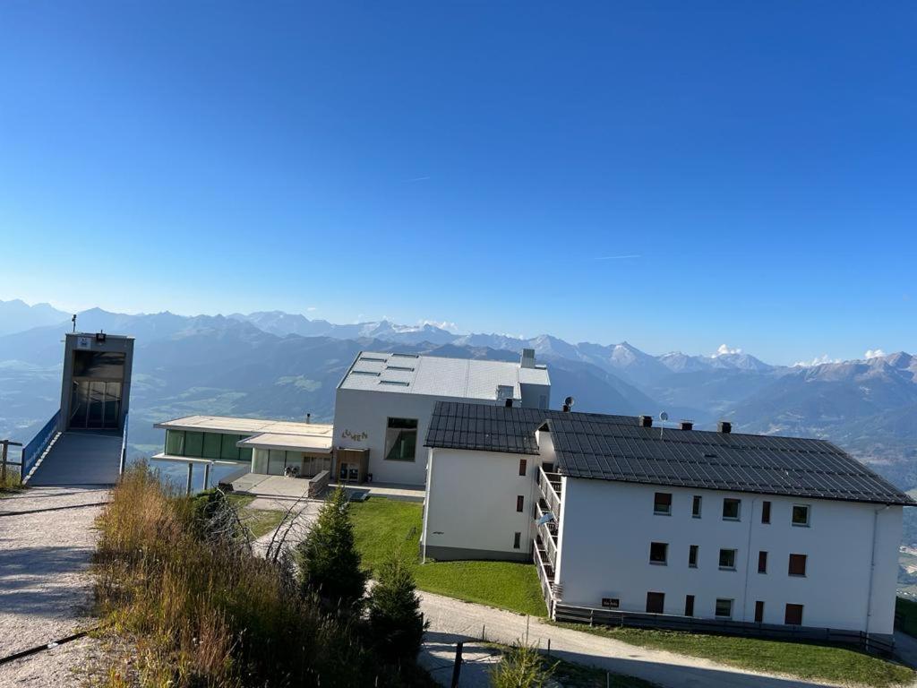 a white building with mountains in the background at Kronplatz Mountain Lodge in Brunico