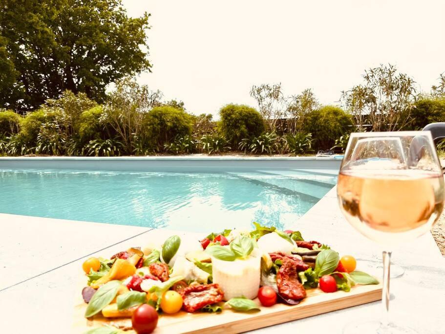 - une assiette de nourriture et un verre de vin à côté de la piscine dans l'établissement Chez Sophie et Vincent, à Le Poiroux