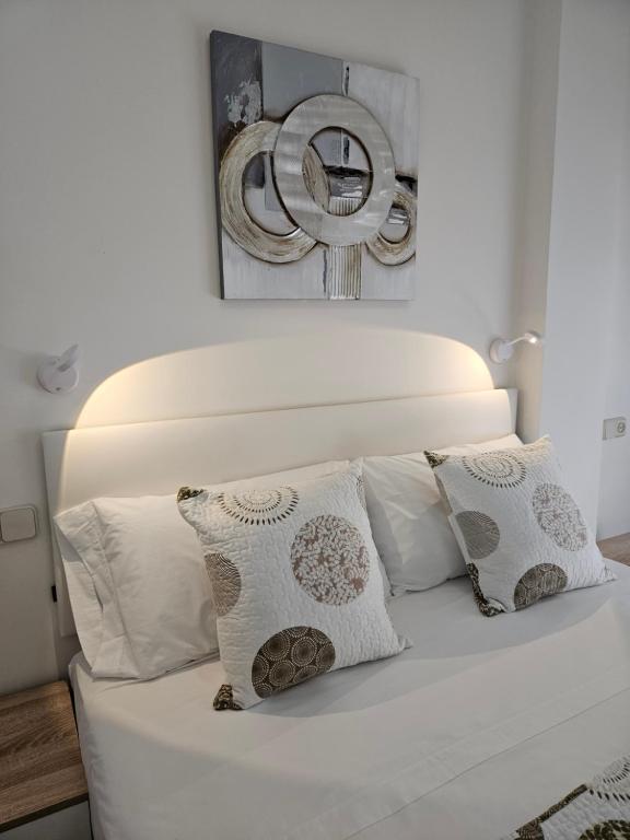 cama blanca con almohadas y espejo en la pared en Apartamento DREAM BAENA en Baena