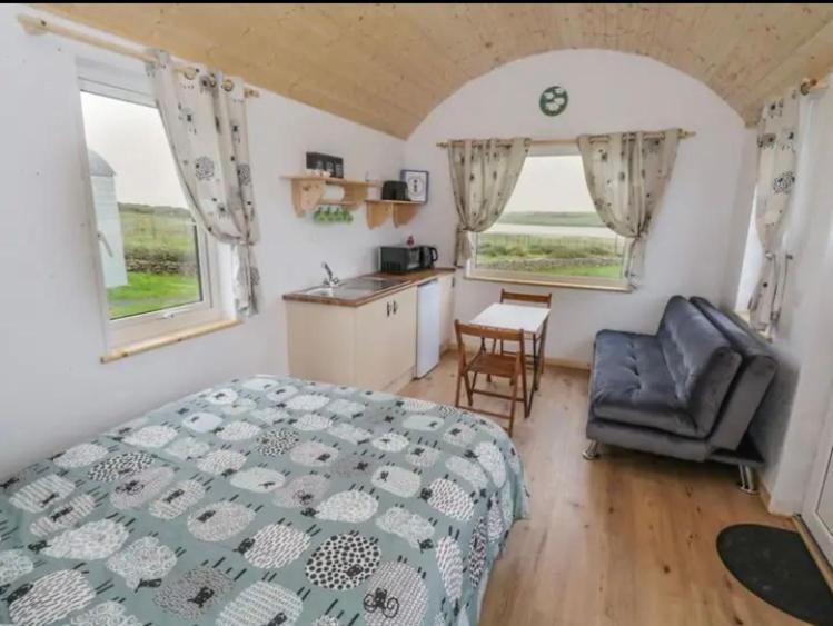 a bedroom with a bed and a chair and two windows at The Snuggly Sheep Farm Stay Shepherd Hut in Ballyshannon