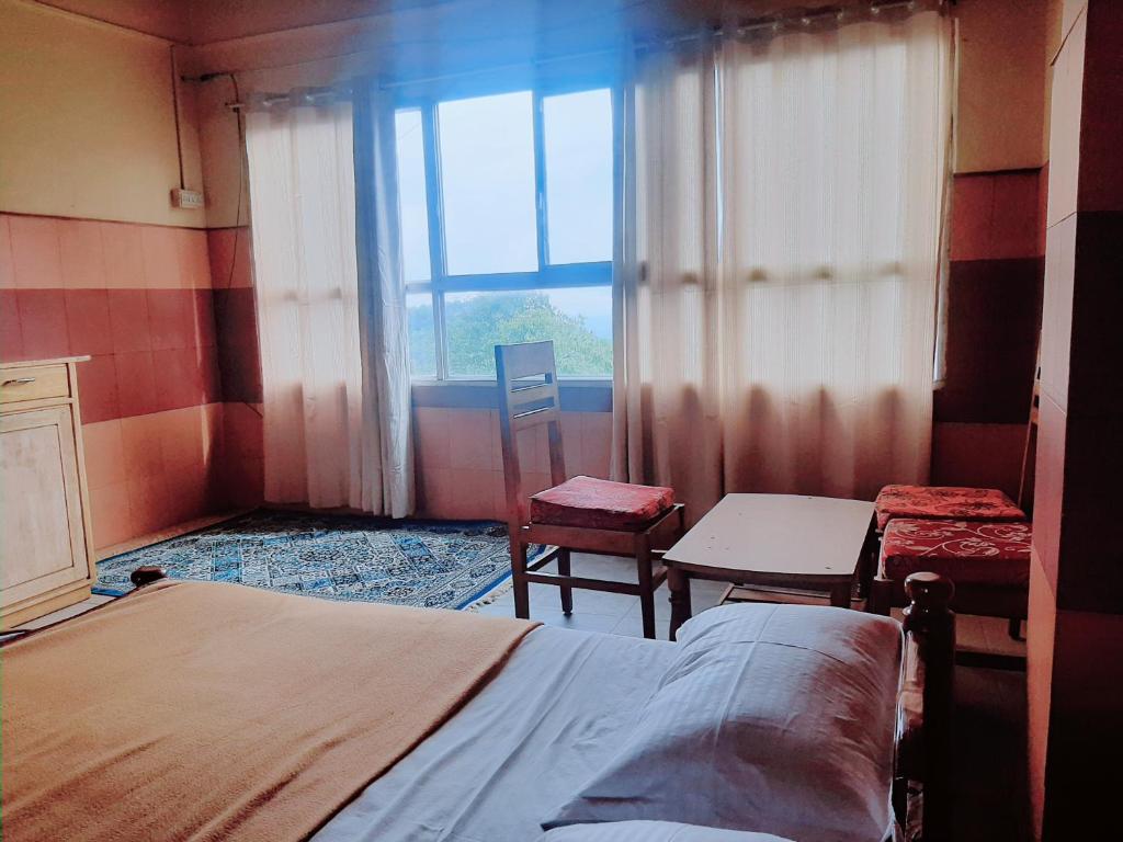 a bedroom with a bed and two chairs and a window at Vega Residency And Bike Rentals in Madikeri