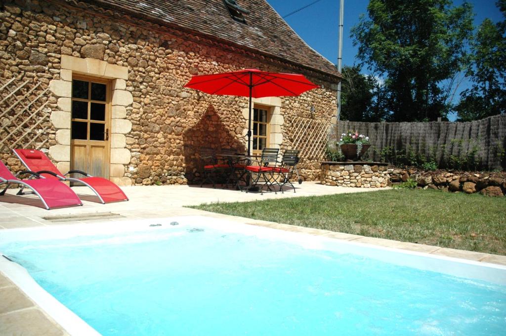 une piscine avec un parasol rouge et des chaises ainsi qu'une maison dans l'établissement Le Lapin sur le Toit - Magnifique grange du XVIIIème, à Rouffignac-Saint-Cernin-de-Reilhac