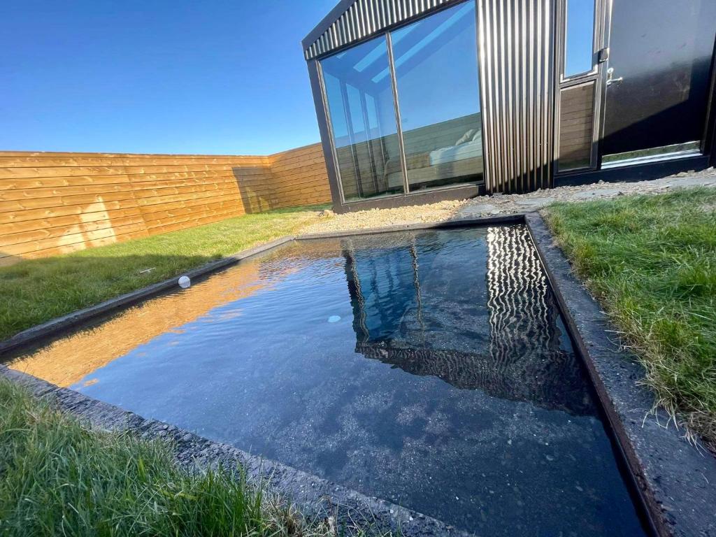 a pool of water in front of a house at Glass roof lodge with private hot tub in Reykholt