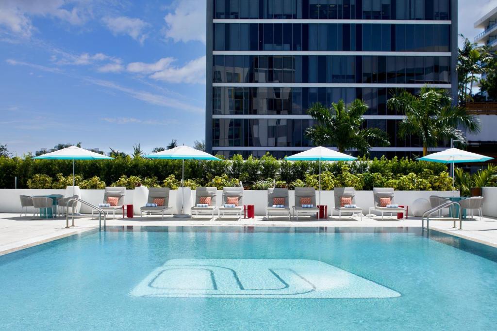 a swimming pool with chairs and umbrellas and a building at Aloft Miami Aventura in Aventura