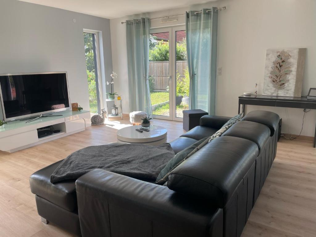 uma sala de estar com um sofá de couro preto e uma televisão em Le gîte de l ill proche Strasbourg em Ostwald