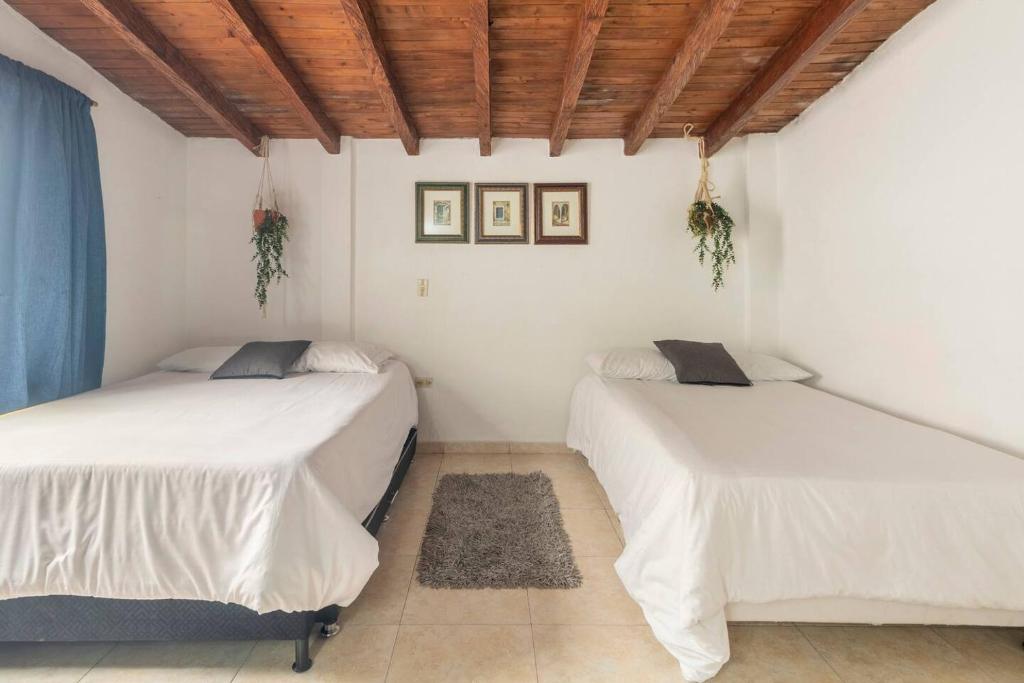 two beds in a room with white walls and wooden ceilings at Letto Hostal in Rionegro