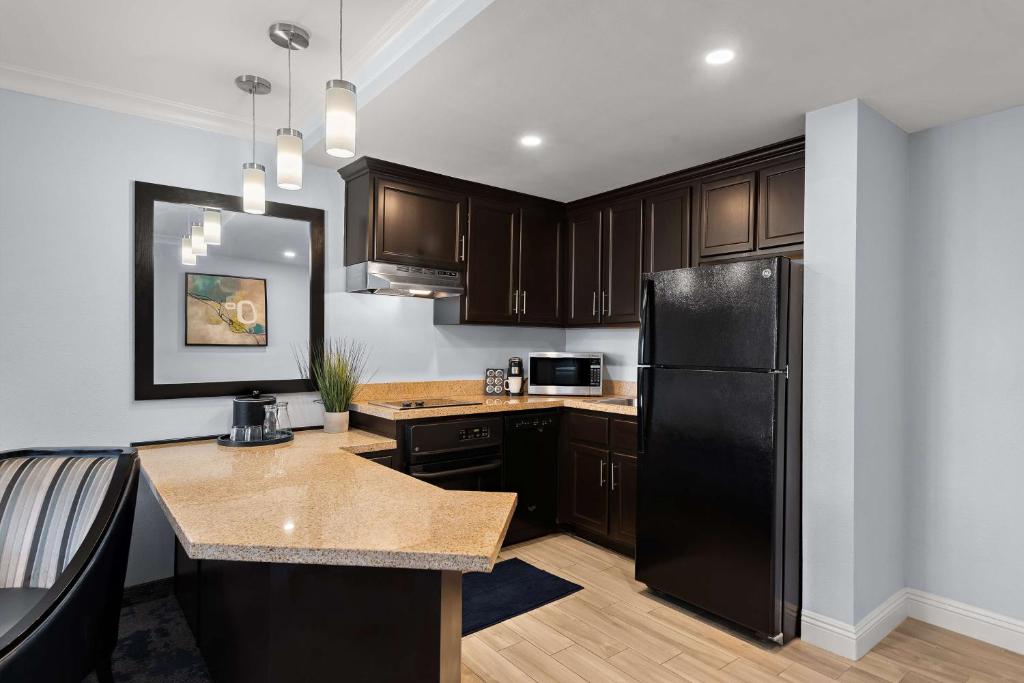 a kitchen with a black refrigerator and wooden cabinets at Best Western Plus Manhattan Beach Hotel in Manhattan Beach