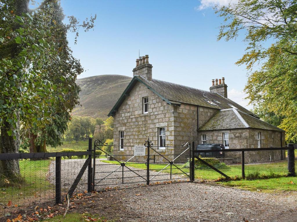 uma velha casa de pedra com um portão em frente em Gleneffock Farmhouse em Tarfside