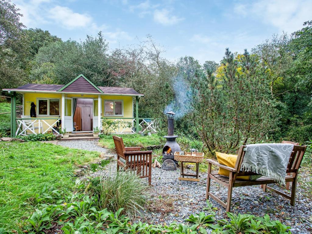 ein kleines gelbes Haus mit Stühlen und einem Kamin in der Unterkunft Laughing Waters in Chillaton