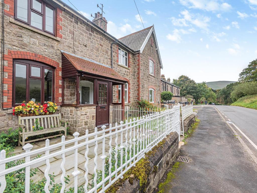 uma casa de tijolos com uma cerca branca ao lado de uma estrada em Veras Cottage em Edale