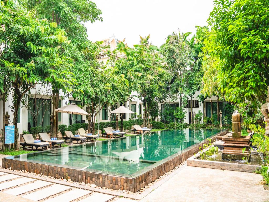 een zwembad in een resort met stoelen en bomen bij Tanei Angkor Resort and Spa in Siem Reap