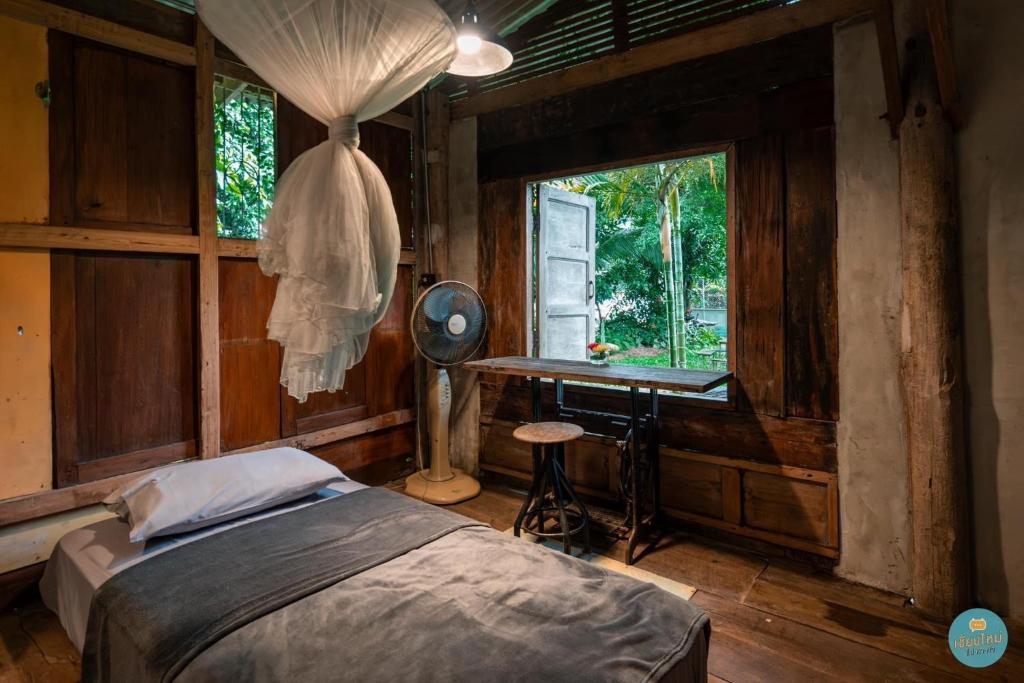 a bedroom with a bed and a desk and a window at Cabinthai in Mae Chaem