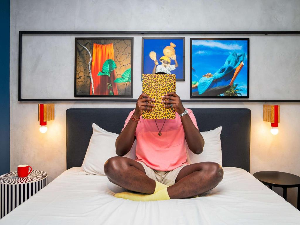 une personne assise sur un lit tenant un morceau de nourriture dans l'établissement Ibis Styles Abidjan Plateau, à Abidjan