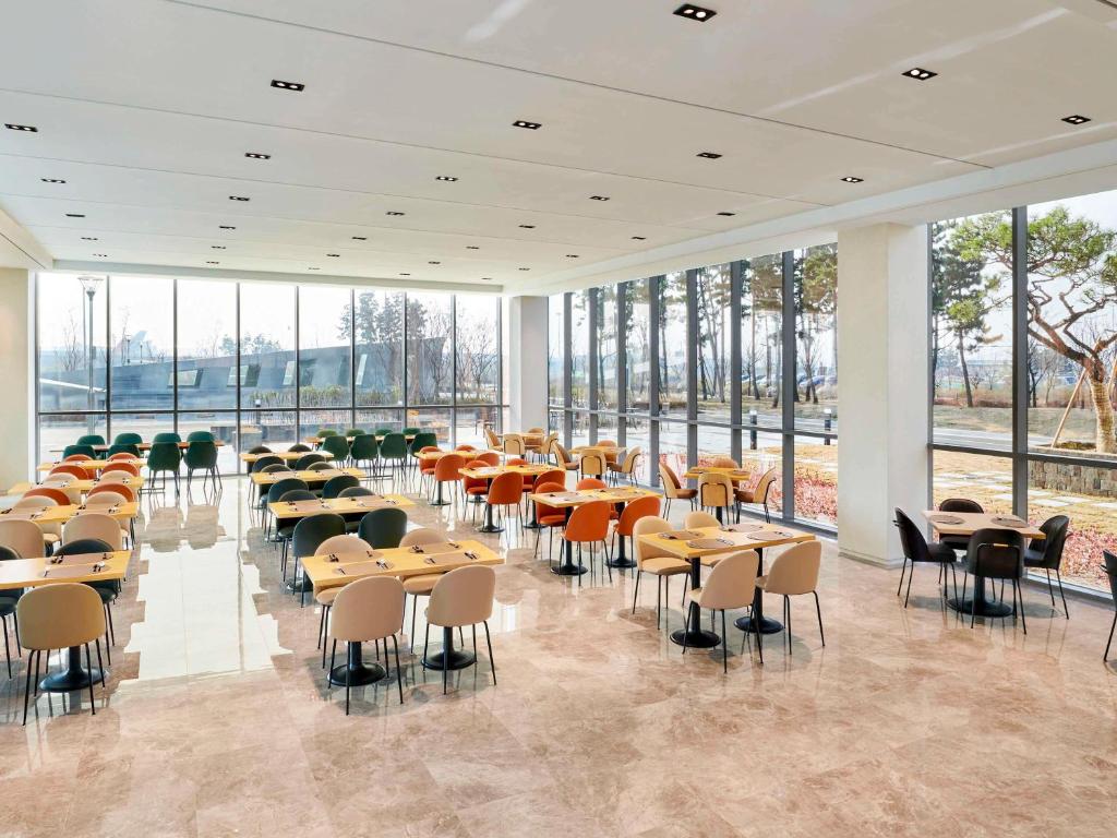 ibis Styles Ambassador Incheon Airport T2 في انشيون: غرفة طعام مع طاولات وكراسي ونوافذ