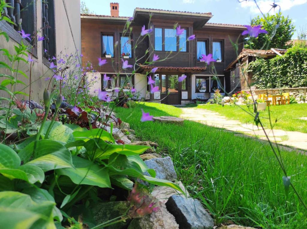 un jardin en face d'une maison ornée de fleurs violettes dans l'établissement Къща ЕТНО, à Koprivchtitsa