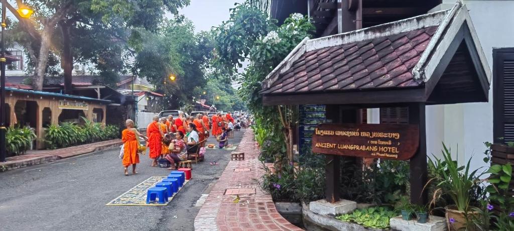 een groep mensen in oranje gewaden die door een straat lopen bij Ancient Luangprabang Hotel in Luang Prabang