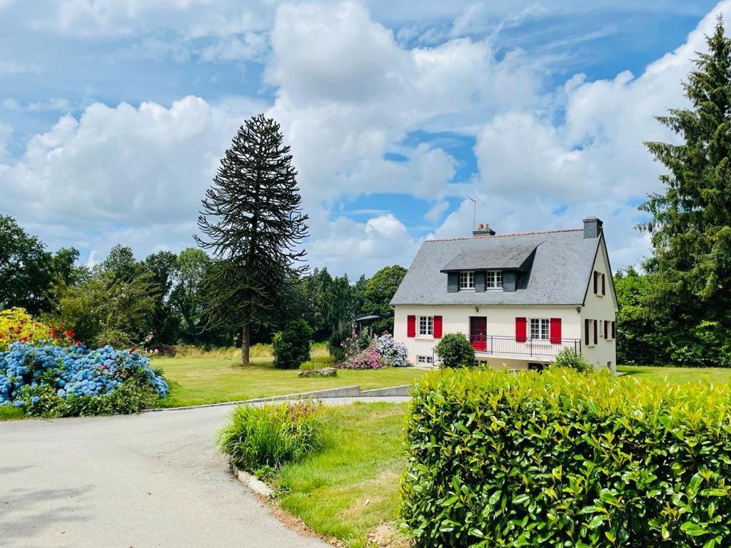 una casa blanca con persianas rojas en una carretera en Maison au calme grand jardin privé aire de jeux Lac de Guerledan en Plouguernével