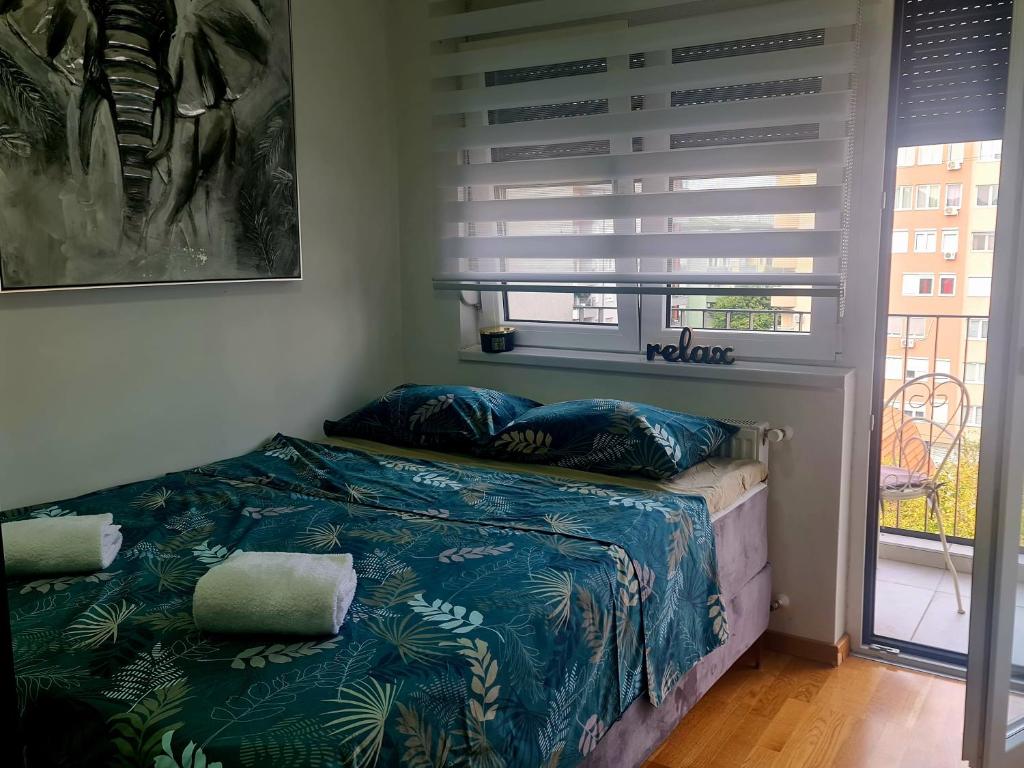 Schlafzimmer mit einem Bett mit blauer Bettwäsche und einem Fenster in der Unterkunft RELAX LUX studio in Jagodina