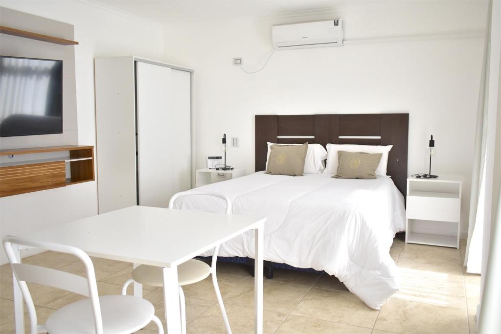 a white bedroom with a white bed and a table at La Gioconda Apart Hotel in Villa María