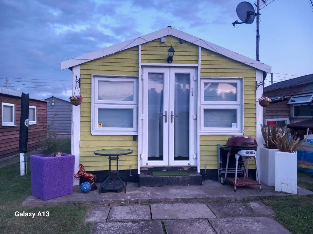 una pequeña casa amarilla con una mesa delante en Tamaras Place en Leysdown-on-Sea