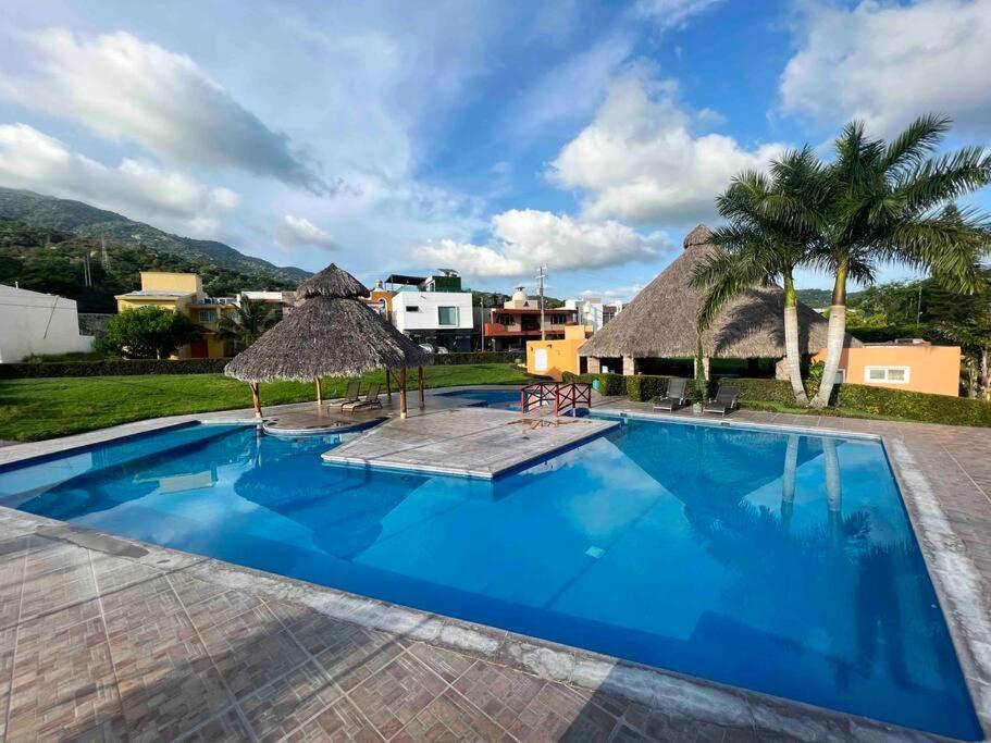 a large blue swimming pool with a thatch roof at Mini Departamento Real del Country Playa Alberca in Manzanillo