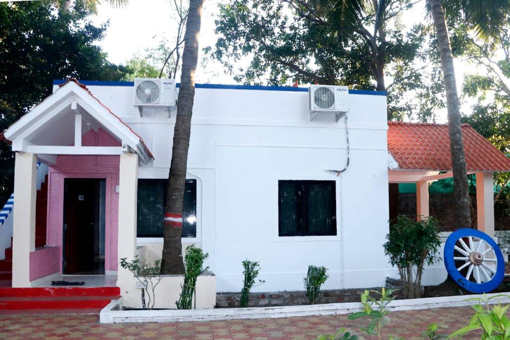 a white house with a red door and trees at White Sand Resort Manori Mumbai Malad West in Mumbai