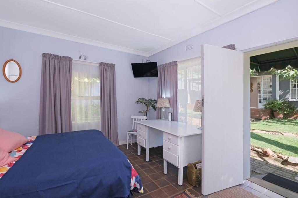 Schlafzimmer mit einem Bett, einem Schreibtisch und einem Fenster in der Unterkunft Sun Garden Cottage in Johannesburg
