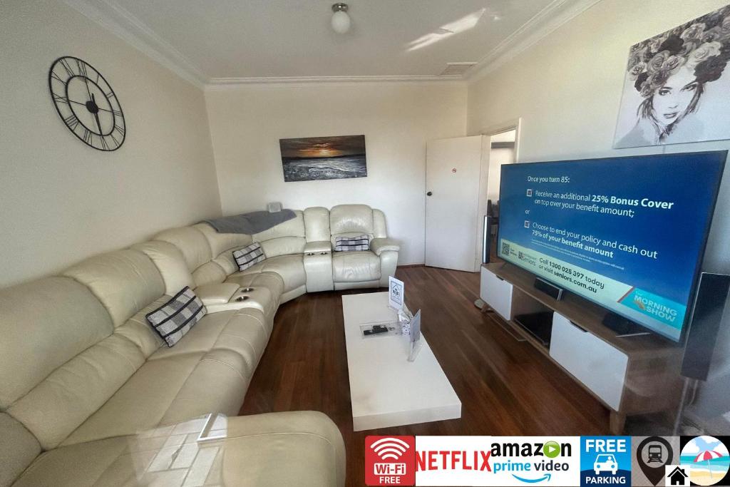 a living room with a large couch and a flat screen tv at Wollongong station holiday house with Wi-Fi,75 Inch TV, Netflix,Parking,Beach in Wollongong