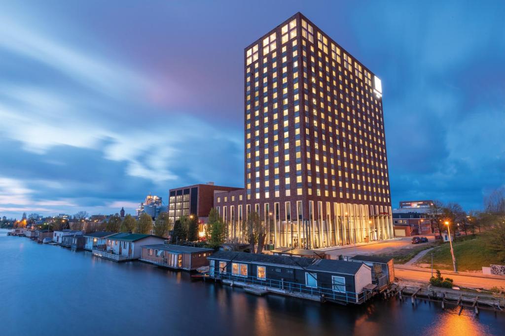 ein hohes Gebäude neben einem Fluss mit einem Gebäude in der Unterkunft Leonardo Royal Hotel Amsterdam in Amsterdam
