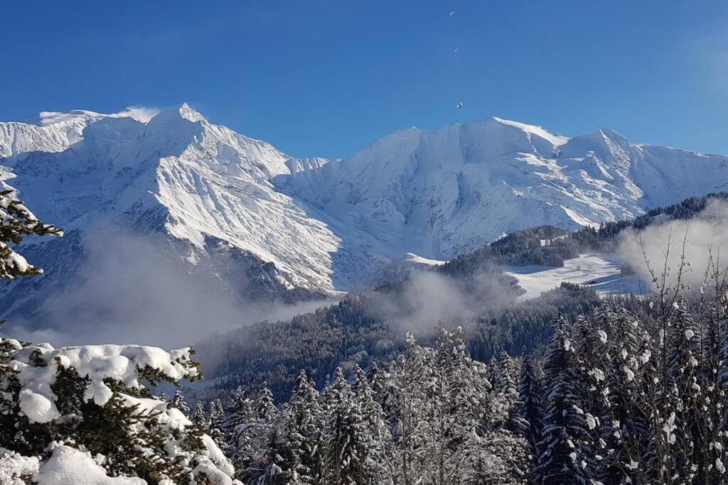 a snow covered mountain range with trees and clouds at Appartement Rémy - at the foot of the slopes in Saint-Gervais-les-Bains