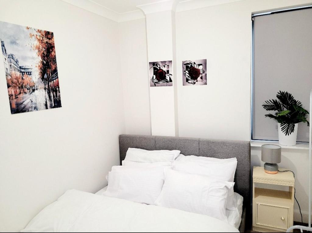 um quarto com paredes brancas e uma cama com almofadas brancas em 2 BEDROOM APT WITH 2 COMFORTABLE KING SIZE BEDs, FREE PRIVATE PARKING, EASY ACCESS TO LONDON em West Byfleet