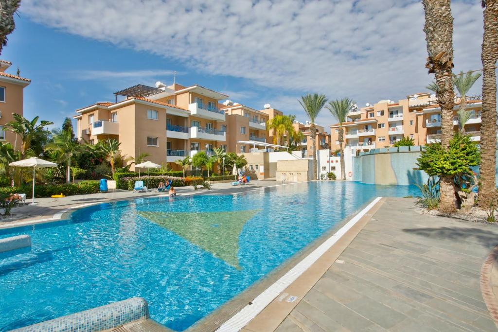 a swimming pool in a resort with palm trees and buildings at Casa Del Sol Townhouse in Iris Village Paphos in Paphos City