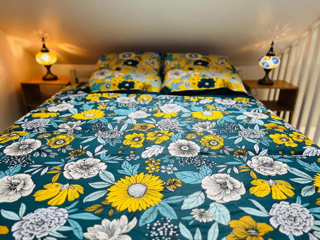 a bed with a blue comforter with yellow and white flowers at Maison Evasion Voyage parking et jardin by Art de Voyager in Étretat